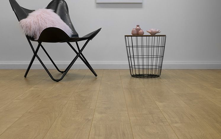 Black chair with pink cushion and wire basket on wooden floor against white wall