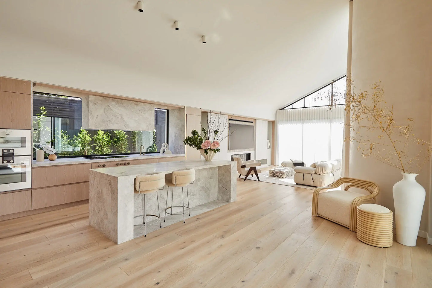 Modern kitchen and living room with wooden flooring and large windows.