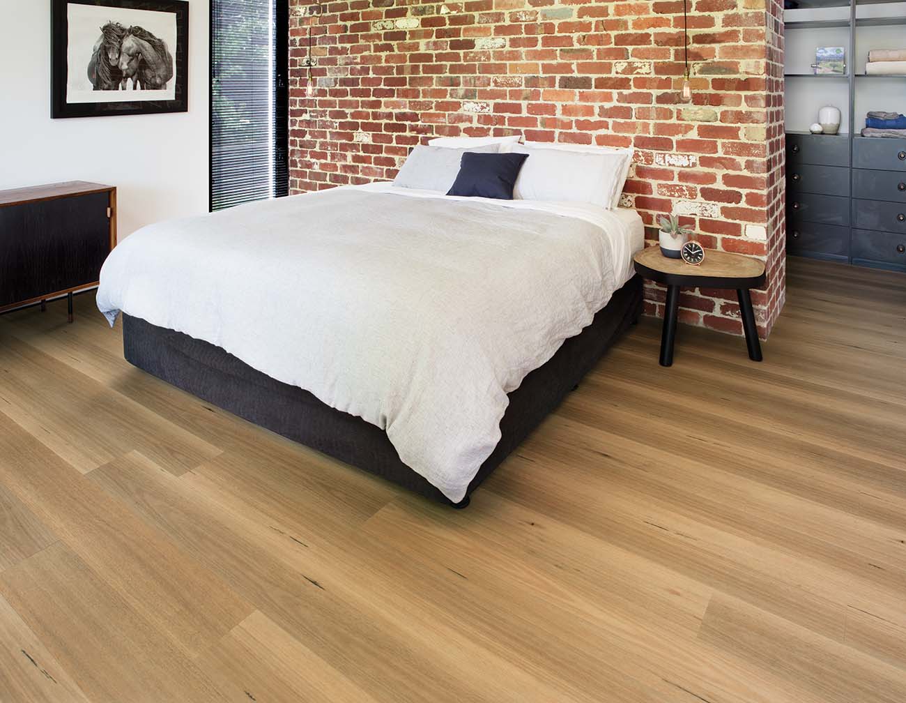 Bedroom with a bed against a brick wall, wooden floor, and side table.
