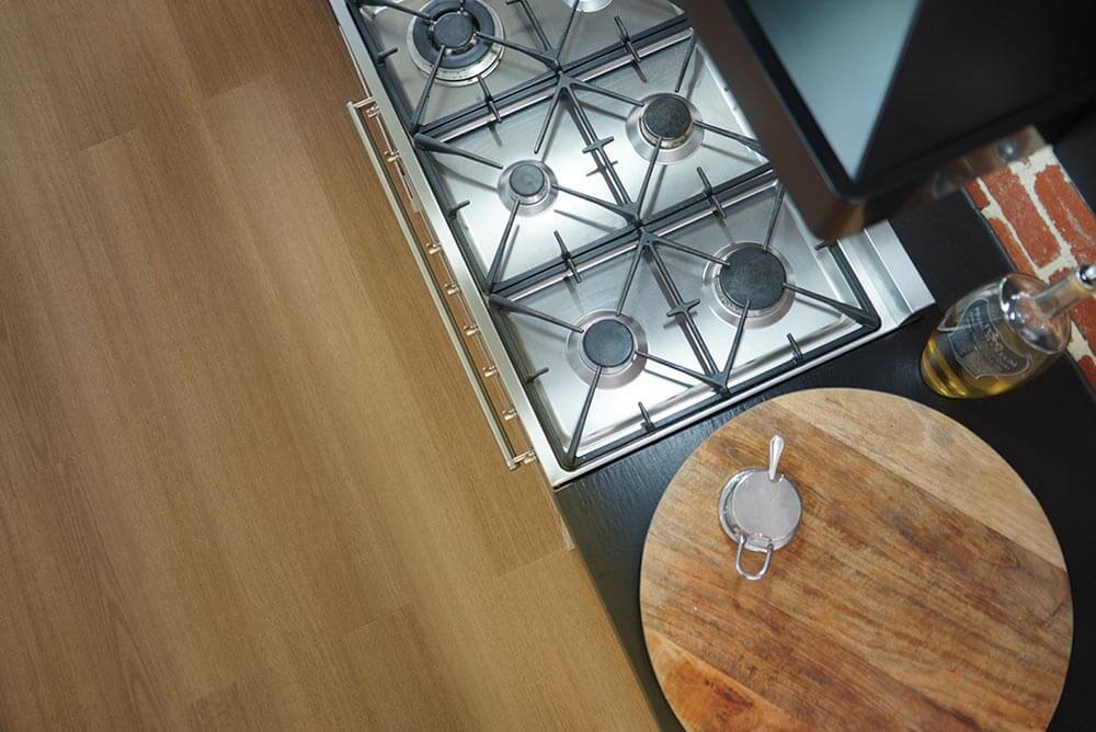 Stainless steel gas stove on a wooden floor with a cutting board and bottle of oil.