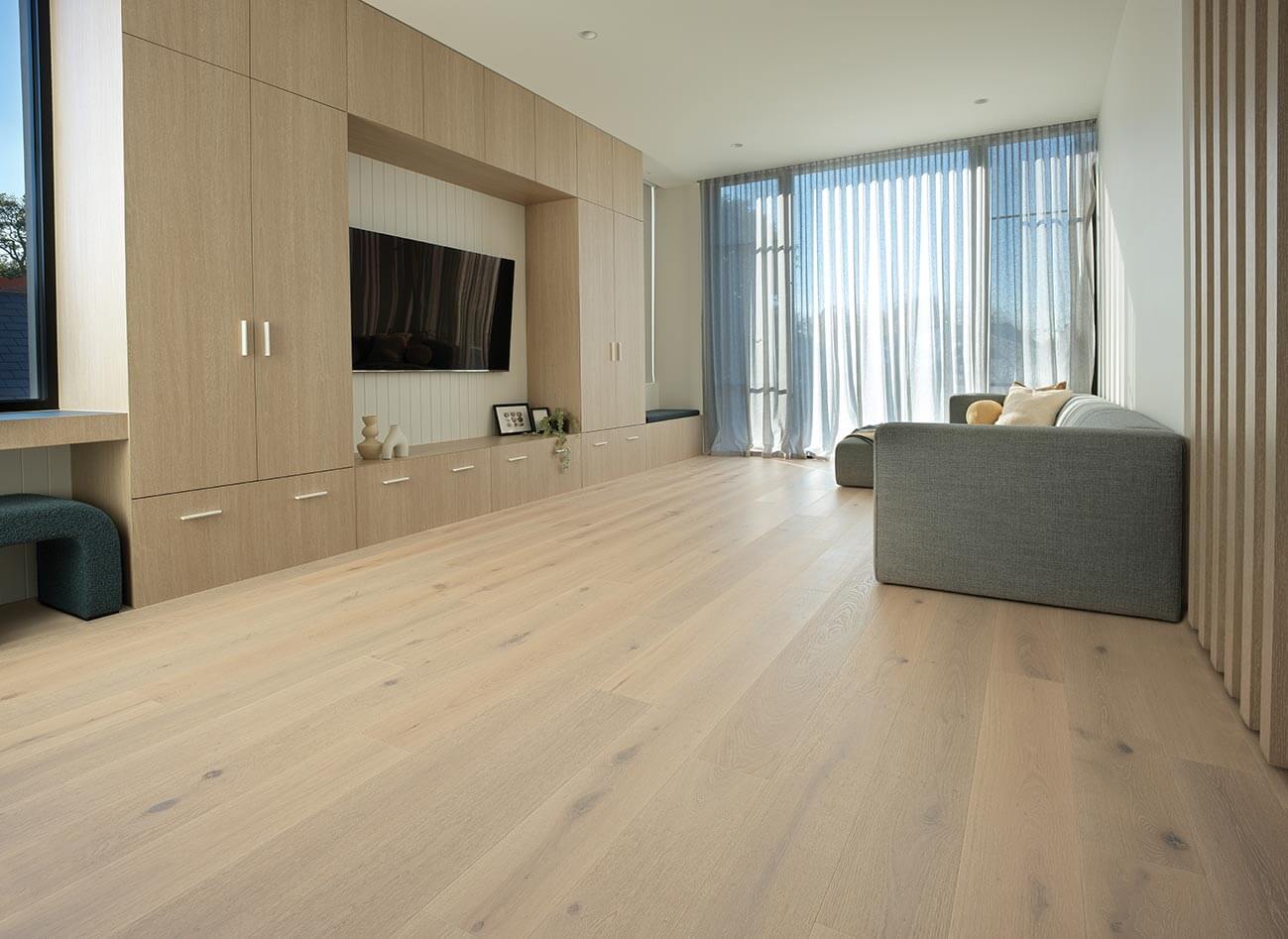 Modern living room with wooden flooring, gray sofa, and large windows.