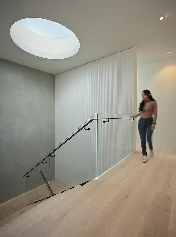 Woman walking up a modern staircase with glass railings in a well-lit interior setting.