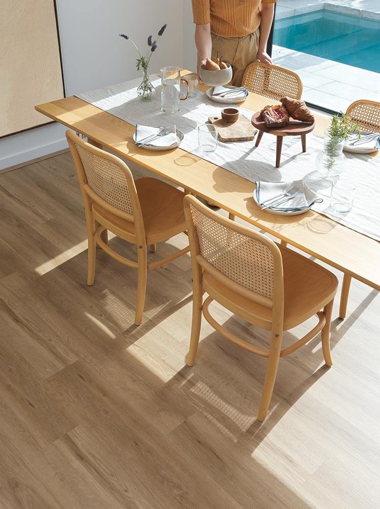 Dining table set with chairs on a wooden floor, pool area in the background