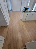 Wooden floor in a room with white walls and a kitchen area.