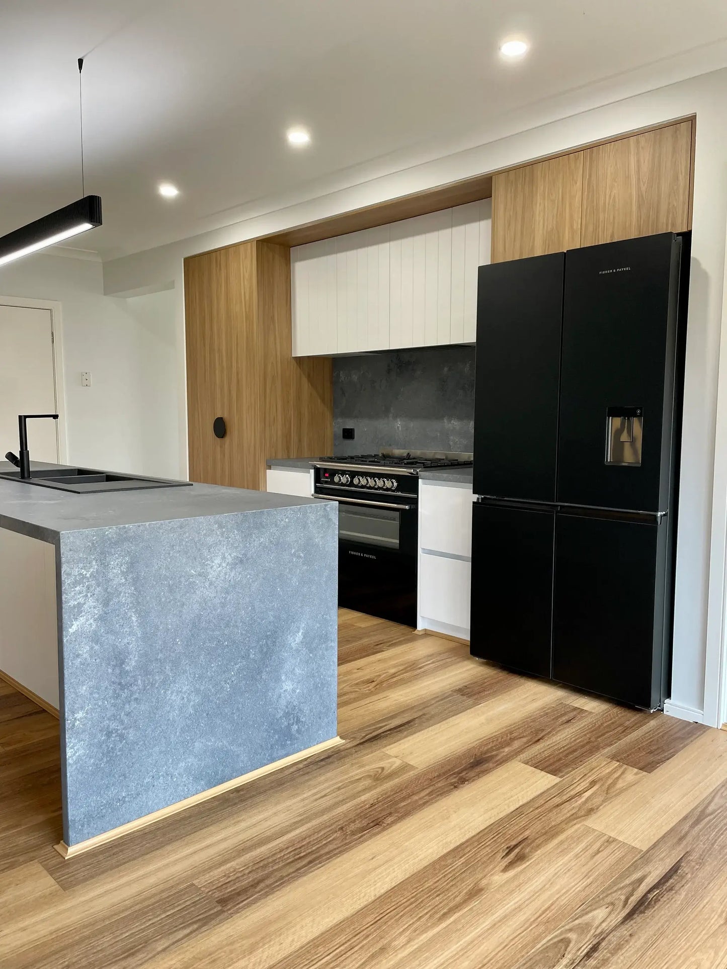 Modern kitchen with black refrigerator, gray island, and wooden flooring.