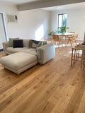 Living room with beige sectional sofa, wooden floor, and dining area in the background.