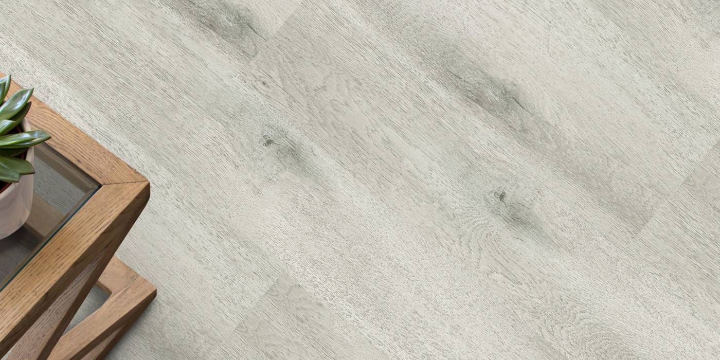 Close-up of a light gray tiled floor with a wooden side table and plant in the corner.