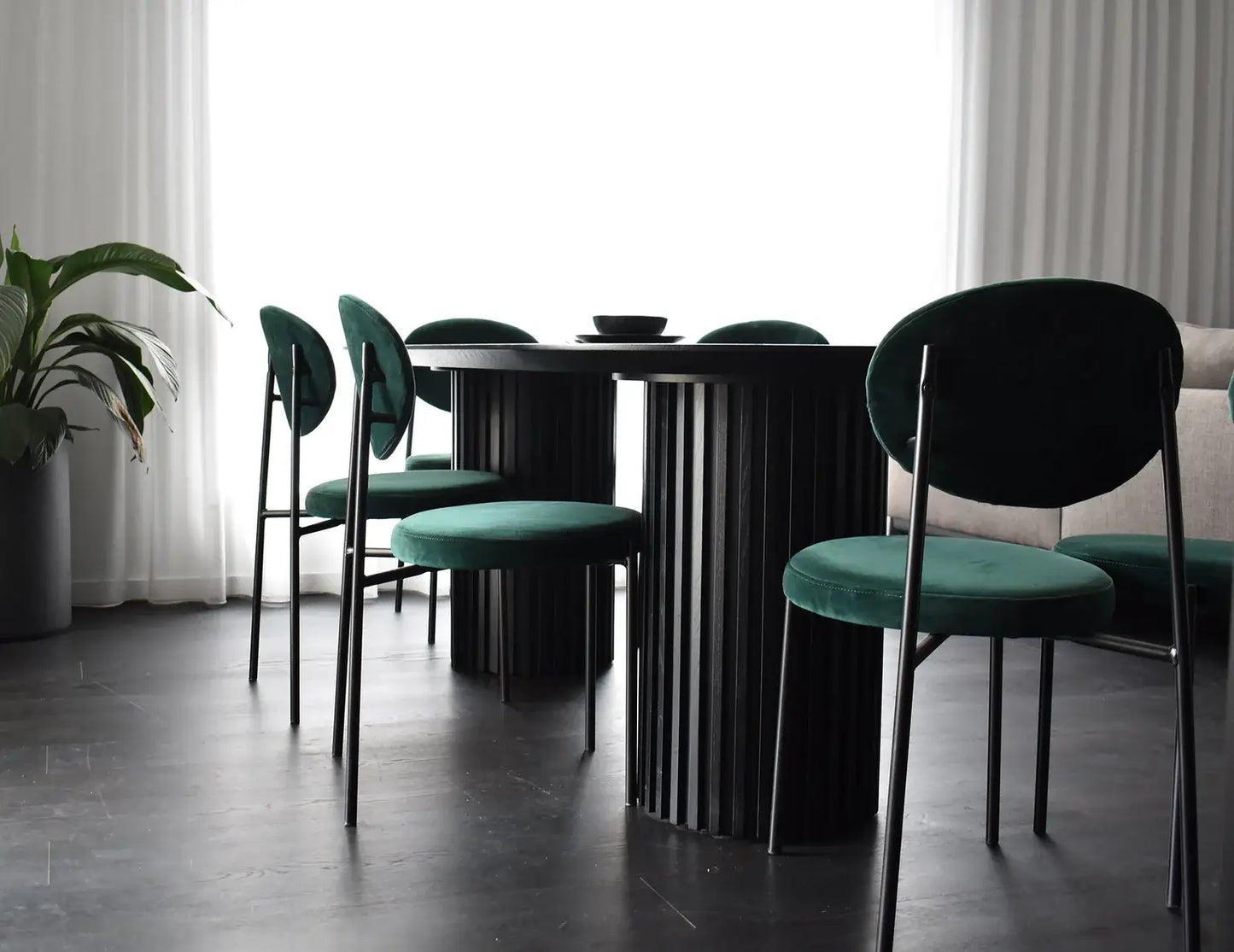 Dining table with green chairs in a room with curtains and a plant.