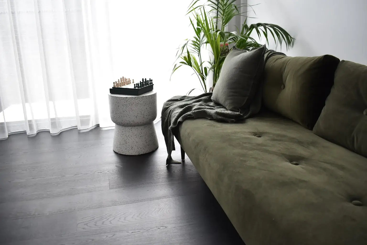 Green sofa with decorative pillows in a room with a plant and small table.