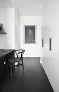 Modern interior with a black chair and desk against a white wall with a framed artwork.
