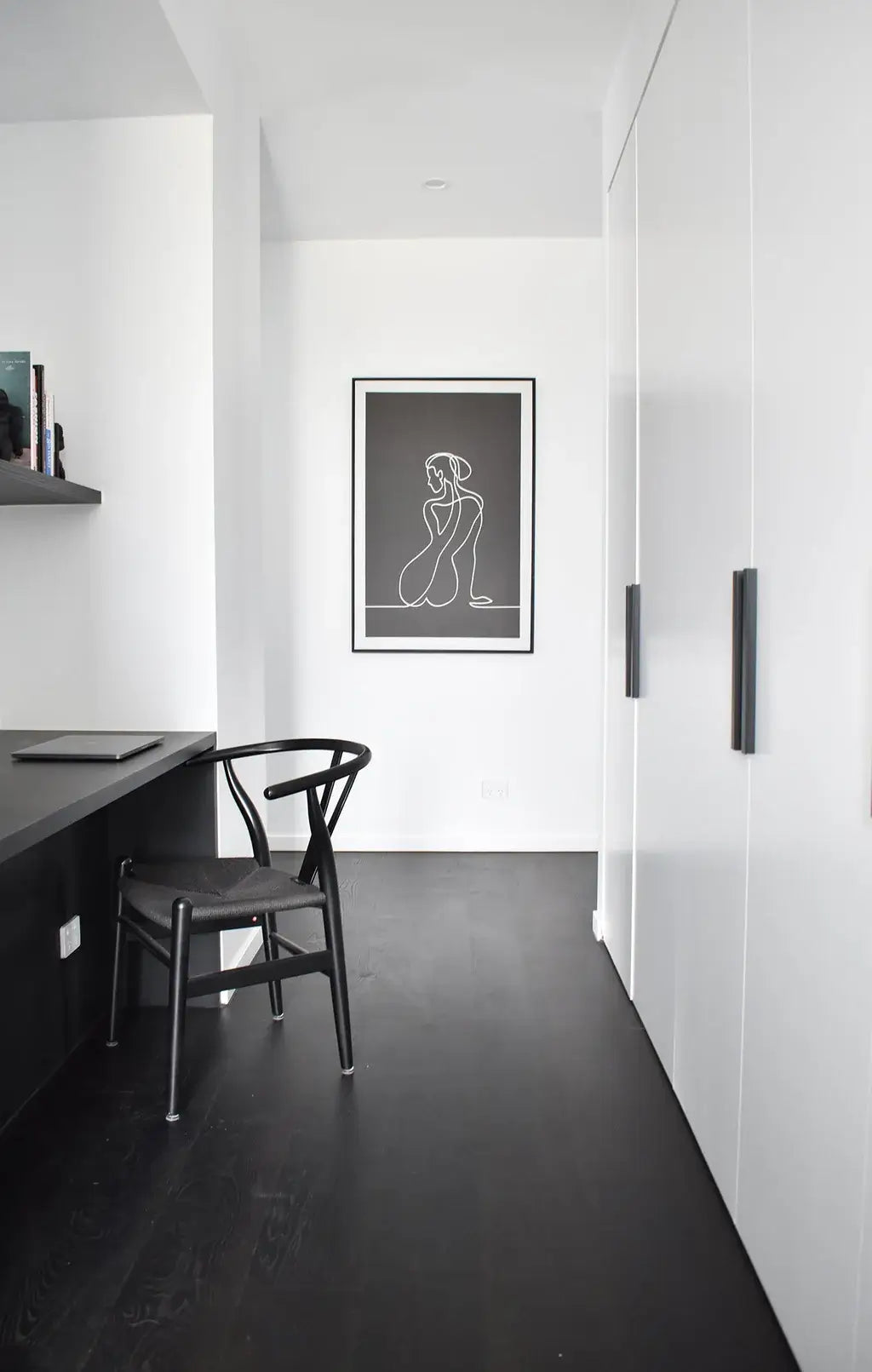 Modern interior with a black chair and desk against a white wall with a framed artwork.